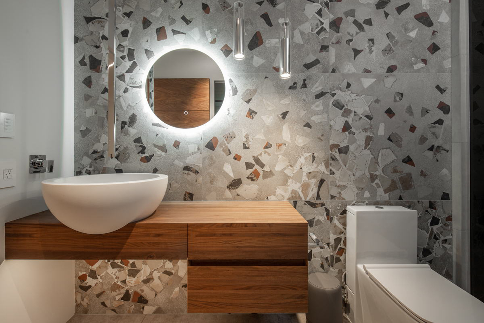 Powder bath with terrazzo tile walls, vessel sink, and backlit round mirror