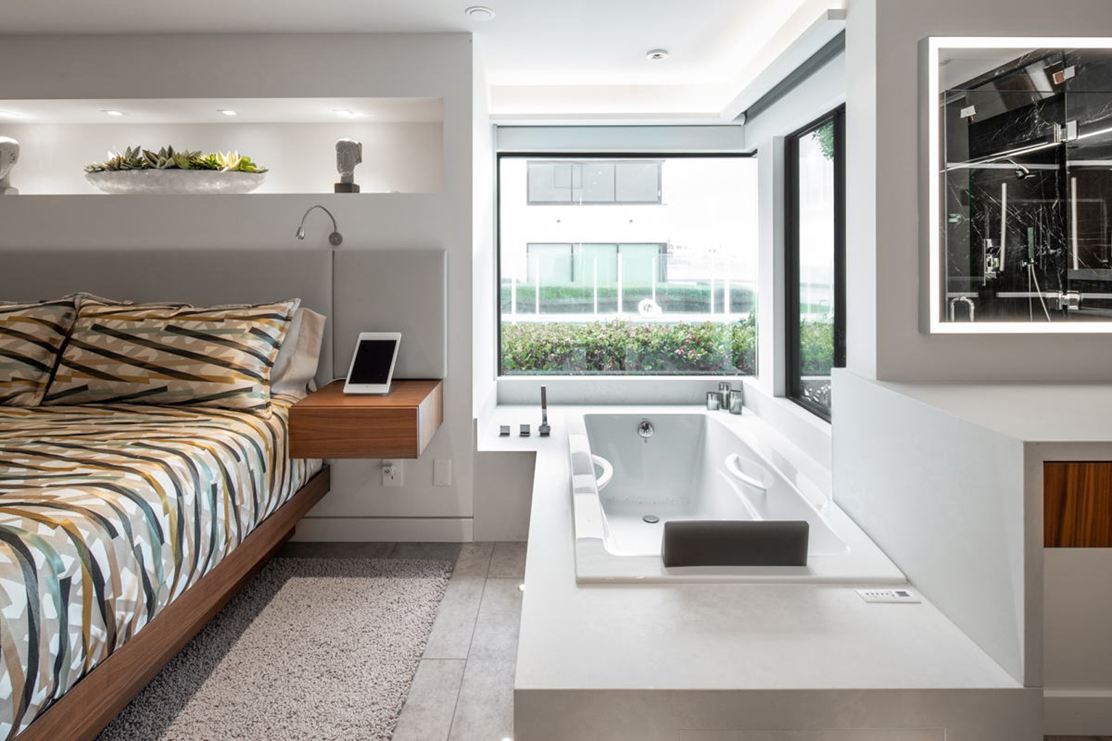Master suite with integrated soaking tub beside bed and garden window